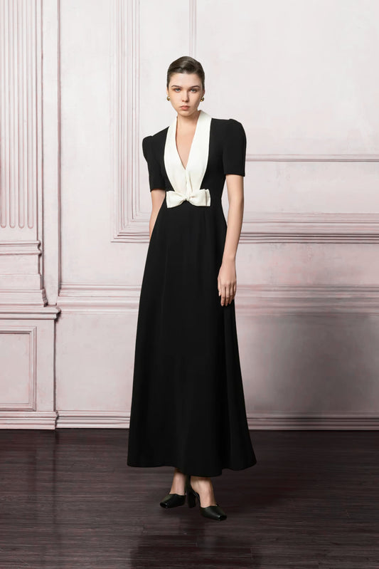 Woman wearing a black dress with a white collar against a light pink wall.