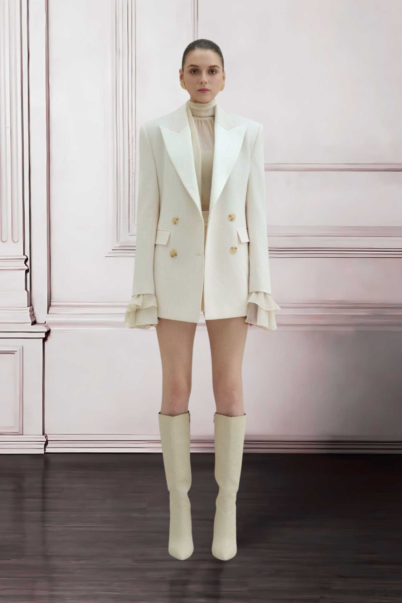 Woman wearing a white blazer and knee-high boots in a room with pink walls.