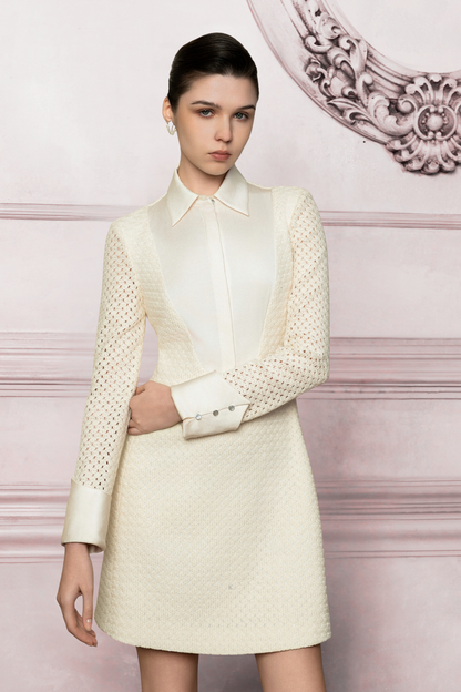 Woman wearing a cream-colored outfit with a textured jacket against a decorative wall.