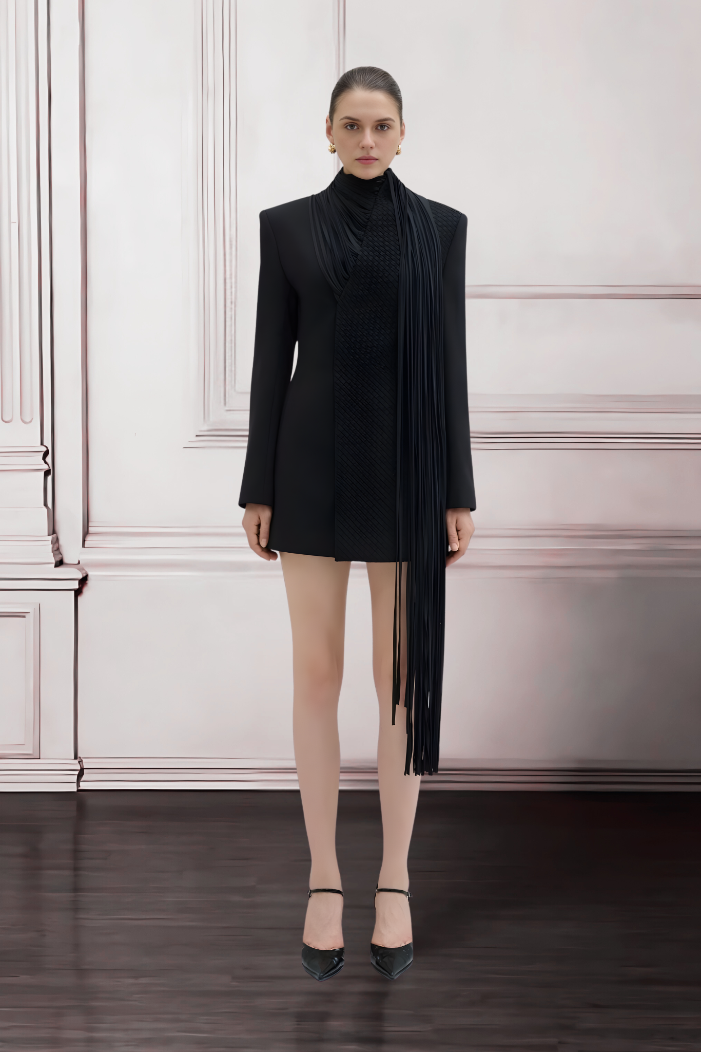 Woman wearing a black dress with a long black scarf against a white wall.