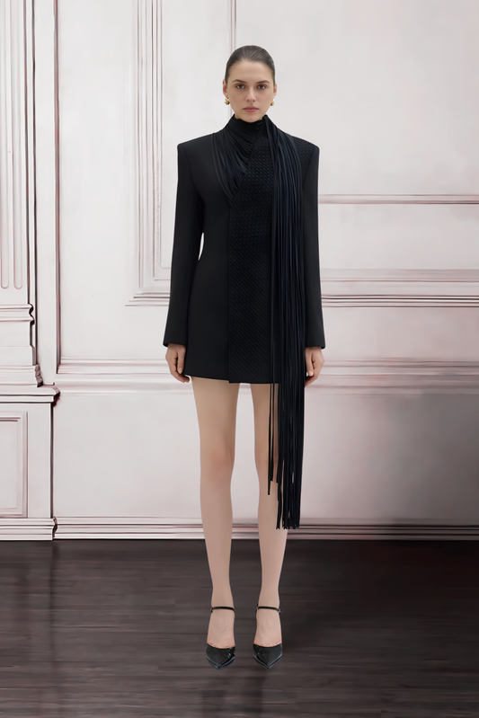 Woman wearing a black dress with a long black scarf against a white wall.