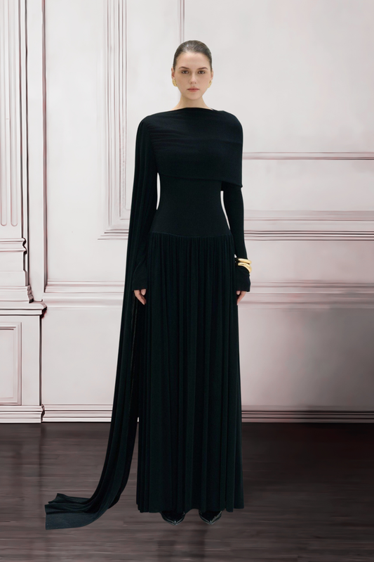 Woman wearing a long black dress with a high slit in a room with white walls and wooden floor.