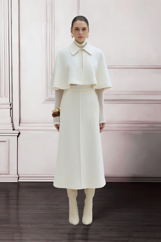 Woman wearing a white outfit with a cape against a pink wall.