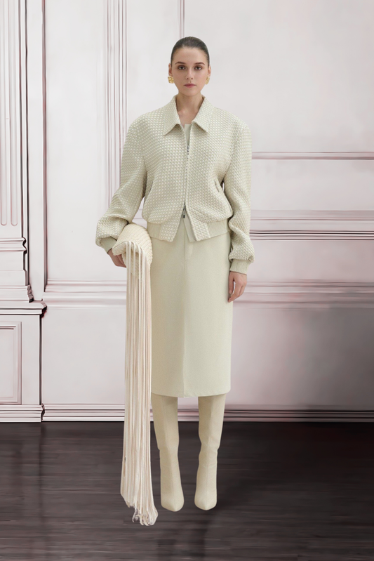 Woman in a light green outfit holding a long white scarf against a white paneled wall.