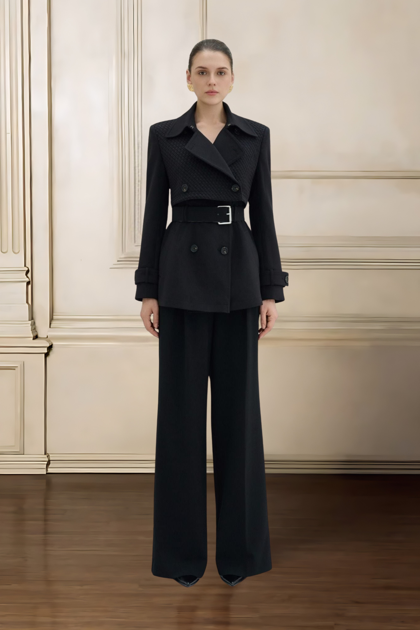 Woman wearing a black suit standing against a beige wall.