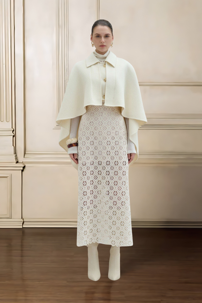 Woman wearing a white outfit with a cape against a beige wall.