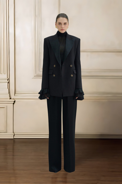 Woman wearing a black suit standing against a beige wall.